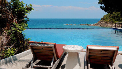 Beach chairs and a table beside a sparkling pool with sea view. Beautiful sunny day at a resort. Concept of leisure and relaxation.