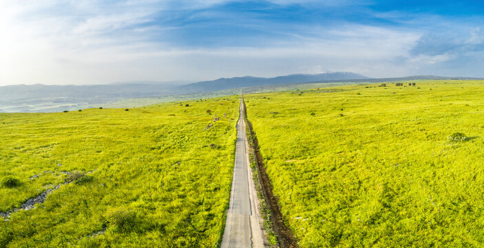 Panoramic aerial view of a straight, endless, road in a grassland setting. Golan Heights, Israel.