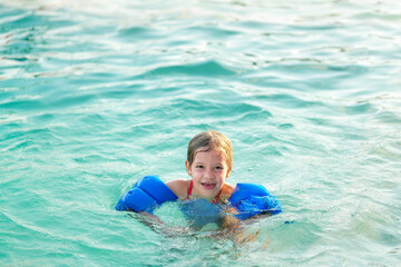Fototapeta na wymiar Niña hermosa feliz rubia latina hispana alegre divertida jugando en el agua en la alberca piscina en el verano y disfrutando de un día soleado al aire libre flotando con sus flotadores