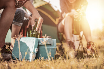 Picnic and camping tent, Adventure, travel, tourism, friendship and recreation Concept. Focus of beer bottles and ice bucket, Group of asian tourists enjoying at camping in the evening.