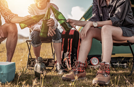 Picnic And Camping Tent, Adventure, Travel, Tourism, Friendship And Recreation Concept. Focus Of Beer Bottles, Group Of Asian Tourists Clinking Beer Bottles In Camping In The Evening By Riverside.