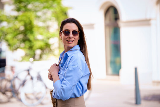 Attractive brown haied woman wearing sunglasses and blue shirt and walking on the street