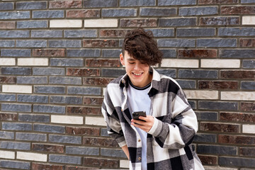 young man reading funny message on phone against a brick wall