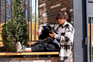 young man looking at something on the phone while sitting on a bench in the city