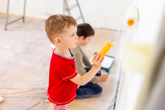Children paint a wall with brush and roller in white color. Children paint wall