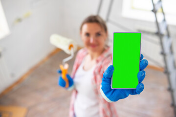 Beautiful woman painter with paint roller showing smartphone with blank screen