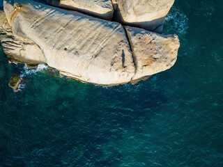 Aerial view of person standing on granite boulder and jumping into sea at Tanote bay, Ko Tao, Thailand.