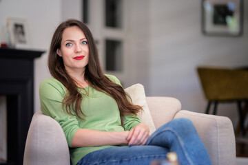 A smiling woman sitting in an armchair in a modern home and relaxing