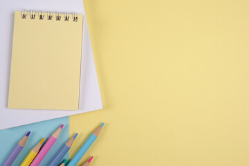 Notepad, sketchbook, colored pencils in soft yellow tones.Products for creativity, schoolchildren, students, teachers.Sale of office supplies for the academic year.Copyspace