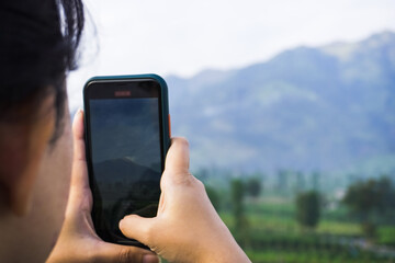 A woman wearing goose down jacket is taking a photo of a mountain and plantation landscape in the...