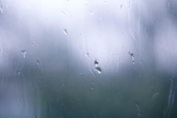 Natural water drops on window. Small medium and large droplets on grey glass. Flowing raindrops. Rainy day.