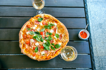 Top view of pizza with fresh basil and cheese, two glasses of white wine on the table in the...