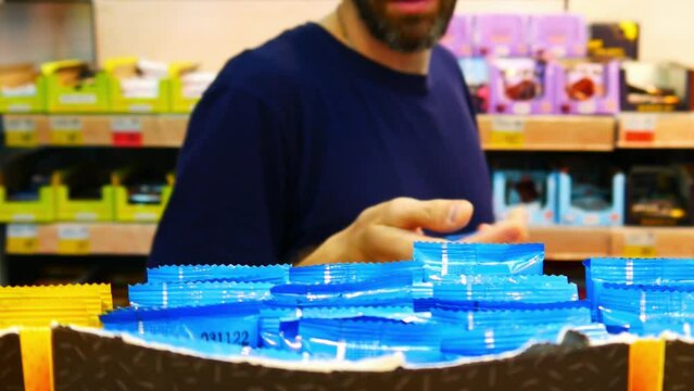 Close-up of many blue chocolate bars on the shelf of a supermarket and a man takes one