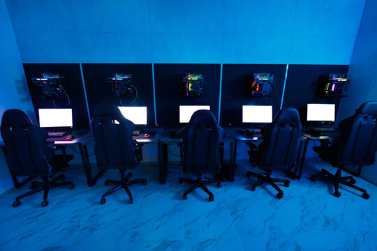 Computer club, monitors, keyboards and headphones in neon lighting, esports equipment.