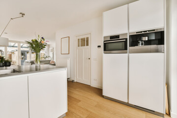a kitchen with wood flooring and white cabinets in the center of the photo is an open door leading to another room