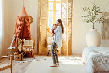Young mother with closed eyes holding little baby in living room with beautiful interior and decor