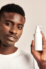 Studio portrait of happy young black guy holding a bottle of facial wash or beauty cream in his...