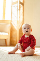 Portrait of small beautiful baby sitting on floor in bedroom at home. Cute child wearing red clothes