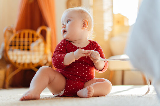 Portrait of little beautiful baby sitting on floor in bedroom at home. Child wearing red clothes