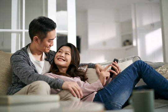 happy young asian couple looking at cellphone pictures together at home