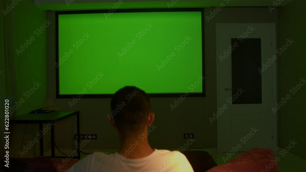 Aufkleber viewing on a projector in a closed room. media. a man looking into a green screen that is shown on a