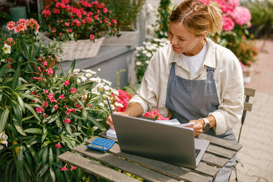 Beautiful flower shop owner wearing apron working on laptop in her store