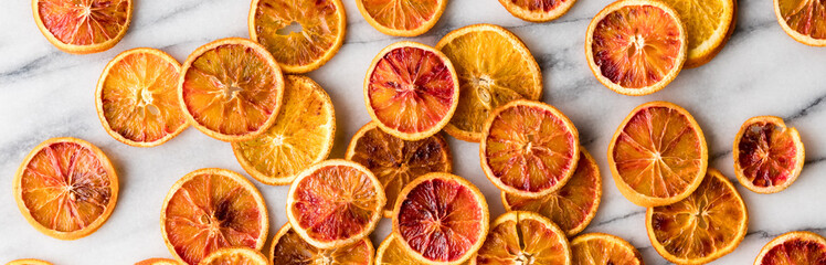 A narrow view of spiced and roasted orange slices spread on a marble slab.