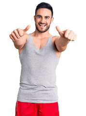 Fototapeta premium Young handsome man wearing swimwear and sleeveless t-shirt approving doing positive gesture with hand, thumbs up smiling and happy for success. winner gesture.