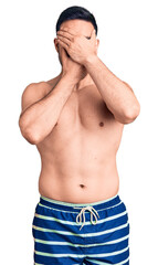 Fototapeta premium Young handsome man wearing swimwear covering eyes and mouth with hands, surprised and shocked. hiding emotion
