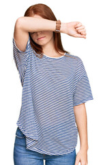 Young read head woman wearing casual clothes and glasses covering eyes with arm, looking serious...