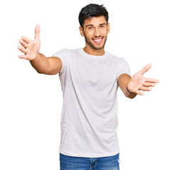 Young handsome man wearing casual white tshirt looking at the camera smiling with open arms for hug. cheerful expression embracing happiness.