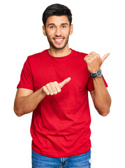 Young handsome man wearing casual red tshirt pointing to the back behind with hand and thumbs up, smiling confident