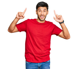 Young handsome man wearing casual red tshirt smiling amazed and surprised and pointing up with fingers and raised arms.