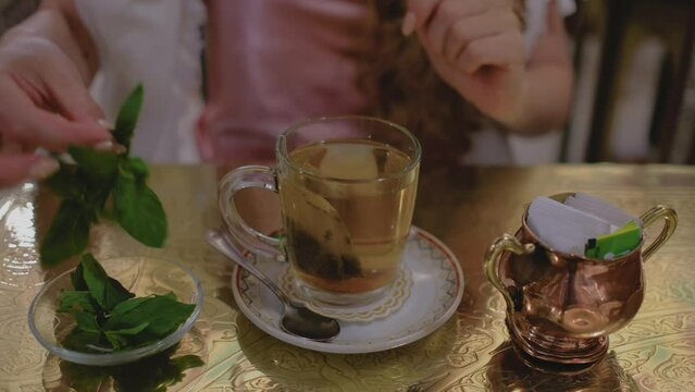 Oriental mint tea in a glass. Female hand putting a green mint leaves.