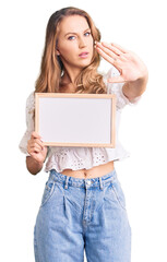 Fototapeta premium Young caucasian woman with blond hair holding blank empty banner with open hand doing stop sign with serious and confident expression, defense gesture