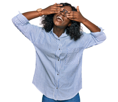 Beautiful african young woman wearing casual clothes and glasses covering eyes with hands smiling cheerful and funny. blind concept.