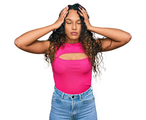 Young hispanic woman with curly hair wearing pink top suffering from headache desperate and stressed because pain and migraine. hands on head.