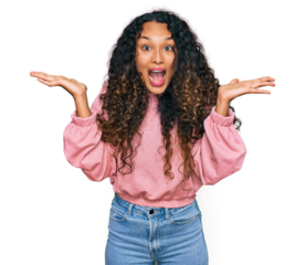 Young hispanic woman with curly hair wearing casual sweatshirt celebrating victory with happy smile and winner expression with raised hands
