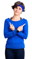 Beautiful young woman with short hair wearing training workout clothes pointing to both sides with fingers, different direction disagree
