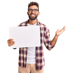 Young hispanic man holding blank empty banner celebrating victory with happy smile and winner expression with raised hands