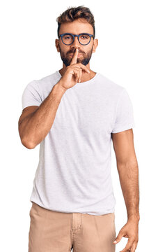Young hispanic man wearing casual clothes and glasses asking to be quiet with finger on lips. silence and secret concept.