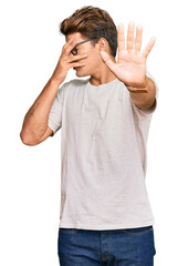 Fototapeta premium Handsome caucasian man wearing casual clothes and glasses covering eyes with hands and doing stop gesture with sad and fear expression. embarrassed and negative concept.