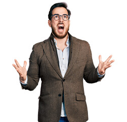 Young hispanic man wearing business jacket and glasses crazy and mad shouting and yelling with aggressive expression and arms raised. frustration concept.