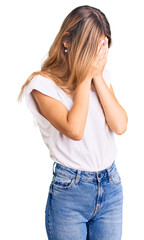 Beautiful caucasian woman with blonde hair wearing casual white tshirt with sad expression covering face with hands while crying. depression concept.