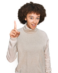 Young hispanic girl wearing wool winter sweater pointing finger up with successful idea. exited and happy. number one.