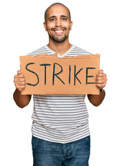 Hispanic adult man holding strike banner cardboard looking positive and happy standing and smiling with a confident smile showing teeth
