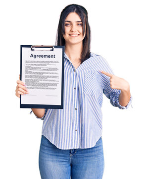 Young beautiful girl holding clipboard with agreement document pointing finger to one self smiling happy and proud