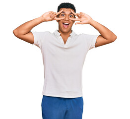 Fototapeta premium Young arab man wearing casual clothes doing peace symbol with fingers over face, smiling cheerful showing victory