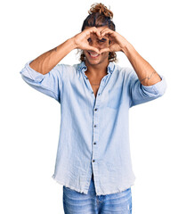 Young hispanic man wearing summer style doing heart shape with hand and fingers smiling looking through sign