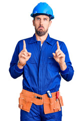 Young handsome man wearing worker uniform and hardhat pointing down looking sad and upset,...